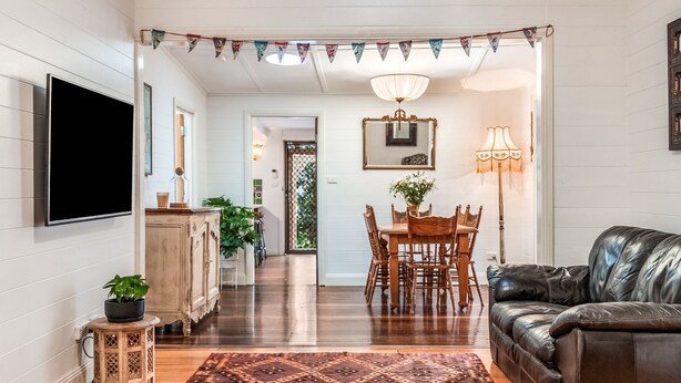 A living room with a flat-screen TV, a wooden dining table with chairs, a leather sofa, and a patterned rug.