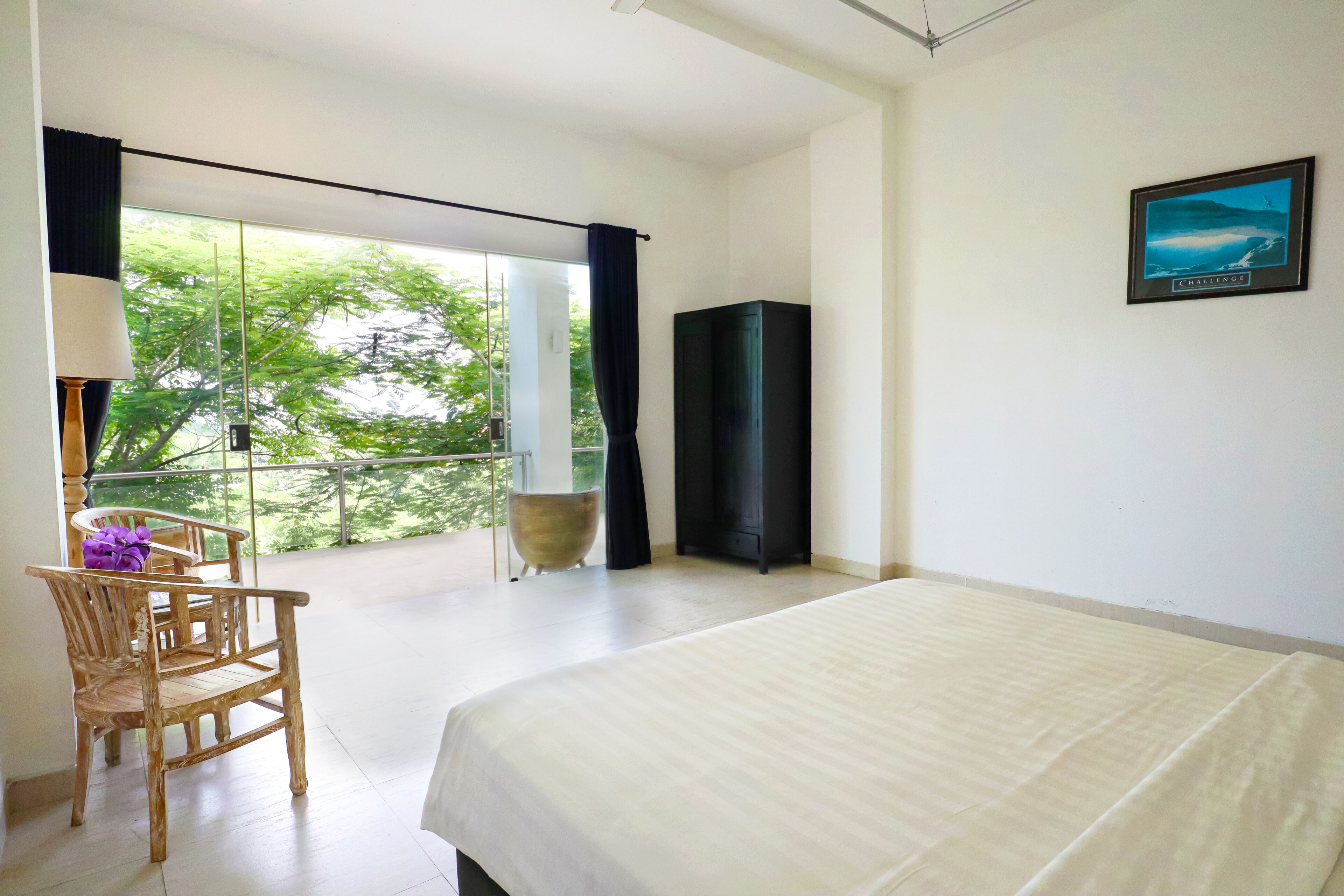 Un dormitorio con una cama grande, una silla, una mesita, un armario negro y una ventana con cortinas.
