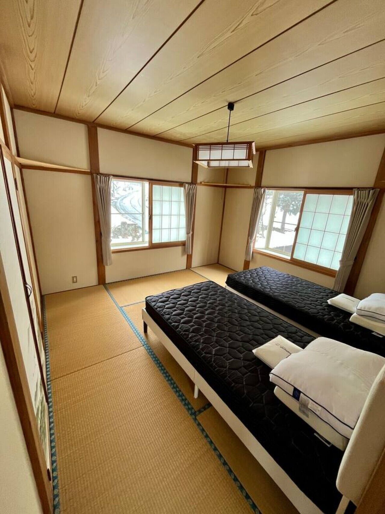 Une pièce de style japonais traditionnel, avec un sol recouvert de tatamis, deux lits, des portes coulissantes et de grandes fenêtres.