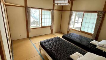 Une pièce de style japonais traditionnel, avec un sol recouvert de tatamis, deux lits, des portes coulissantes et de grandes fenêtres.