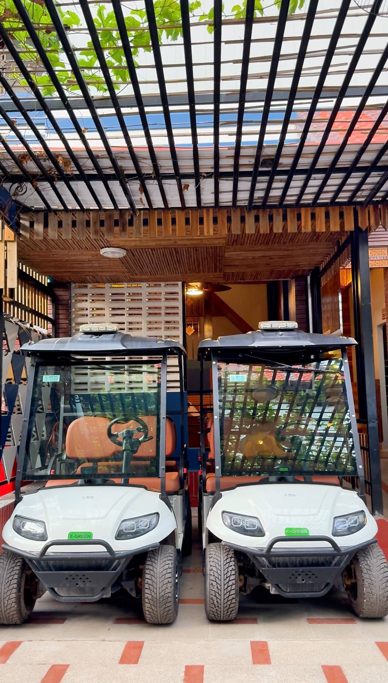 Two white electric golf carts parked under a covered area with a wooden ceiling and a metal grid roof.