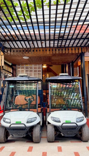 Two white electric golf carts parked under a covered area with a wooden ceiling and a metal grid roof.