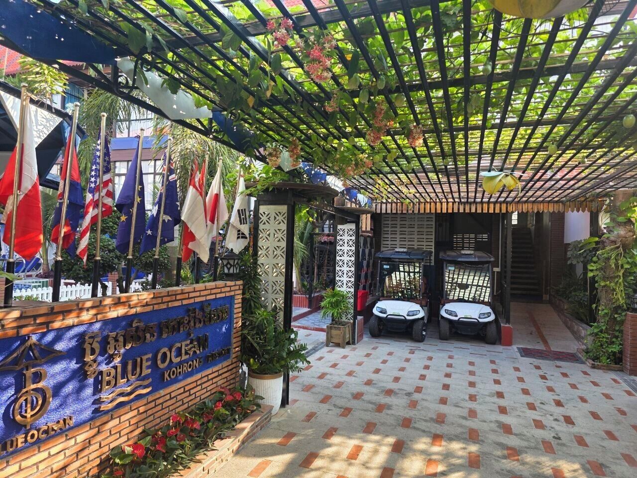 Un espacio al aire libre techado con un letrero que dice 'Blue Ocean Kohron', banderas, un coche blanco y un scooter.