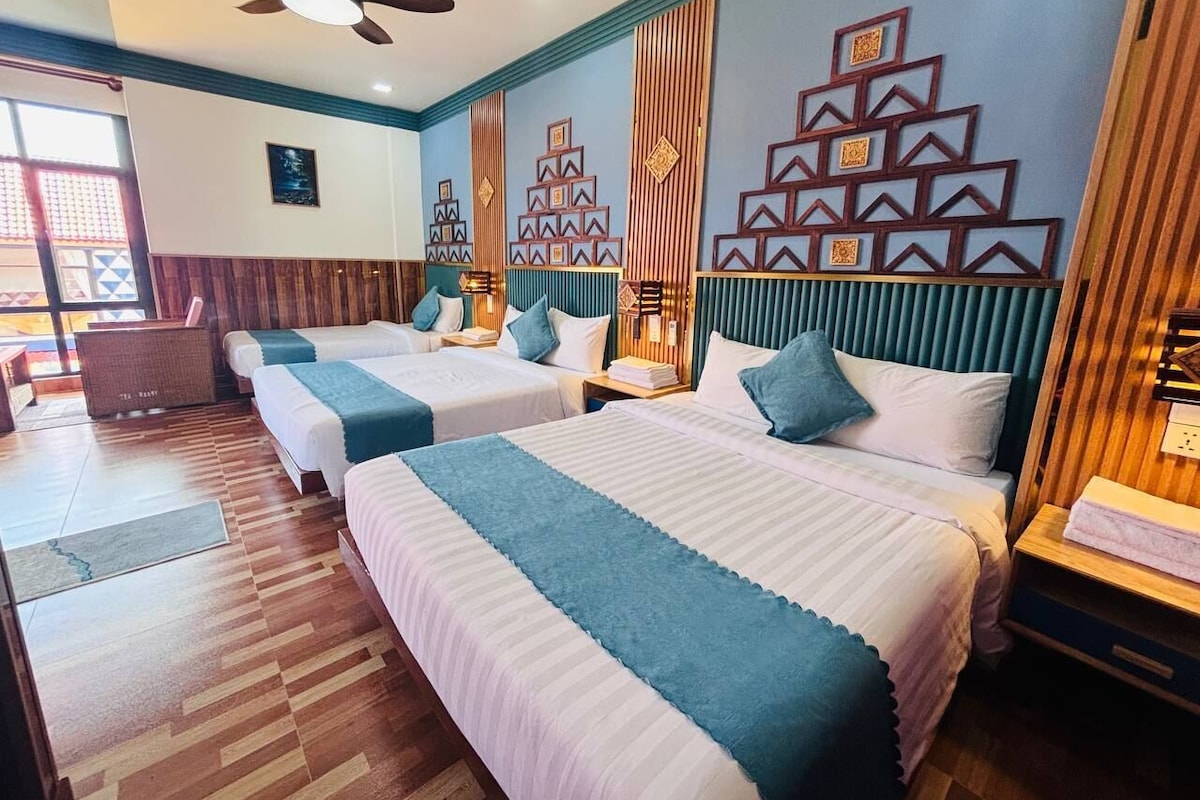 Habitación de hotel con dos camas, piso de madera, ventilador de techo y paneles decorativos en la pared.