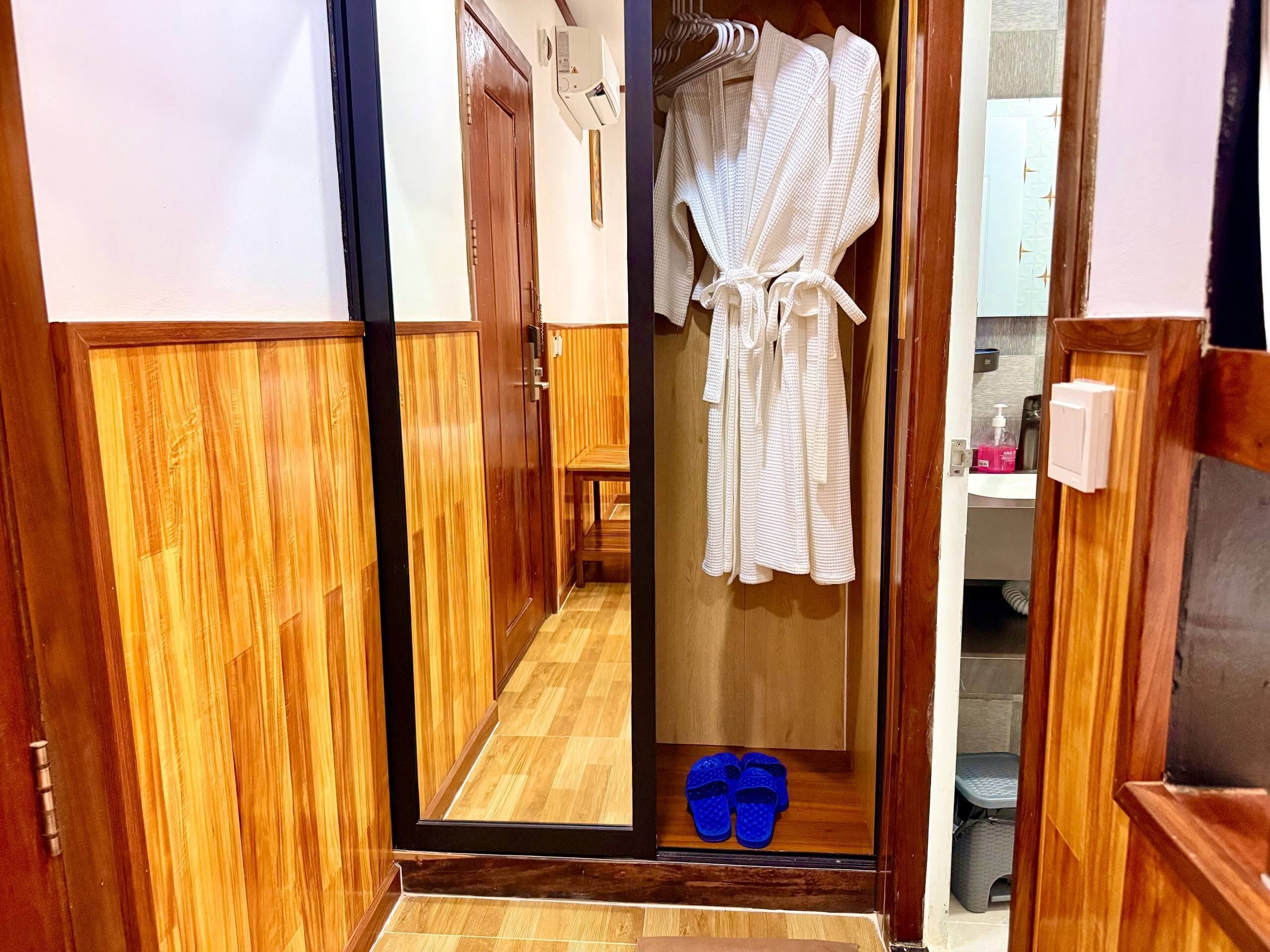 Un couloir en bois, avec un miroir reflétant une robe blanche et des pantoufles bleues.