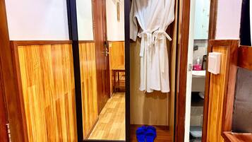 Un couloir en bois, avec un miroir reflétant une robe blanche et des pantoufles bleues.