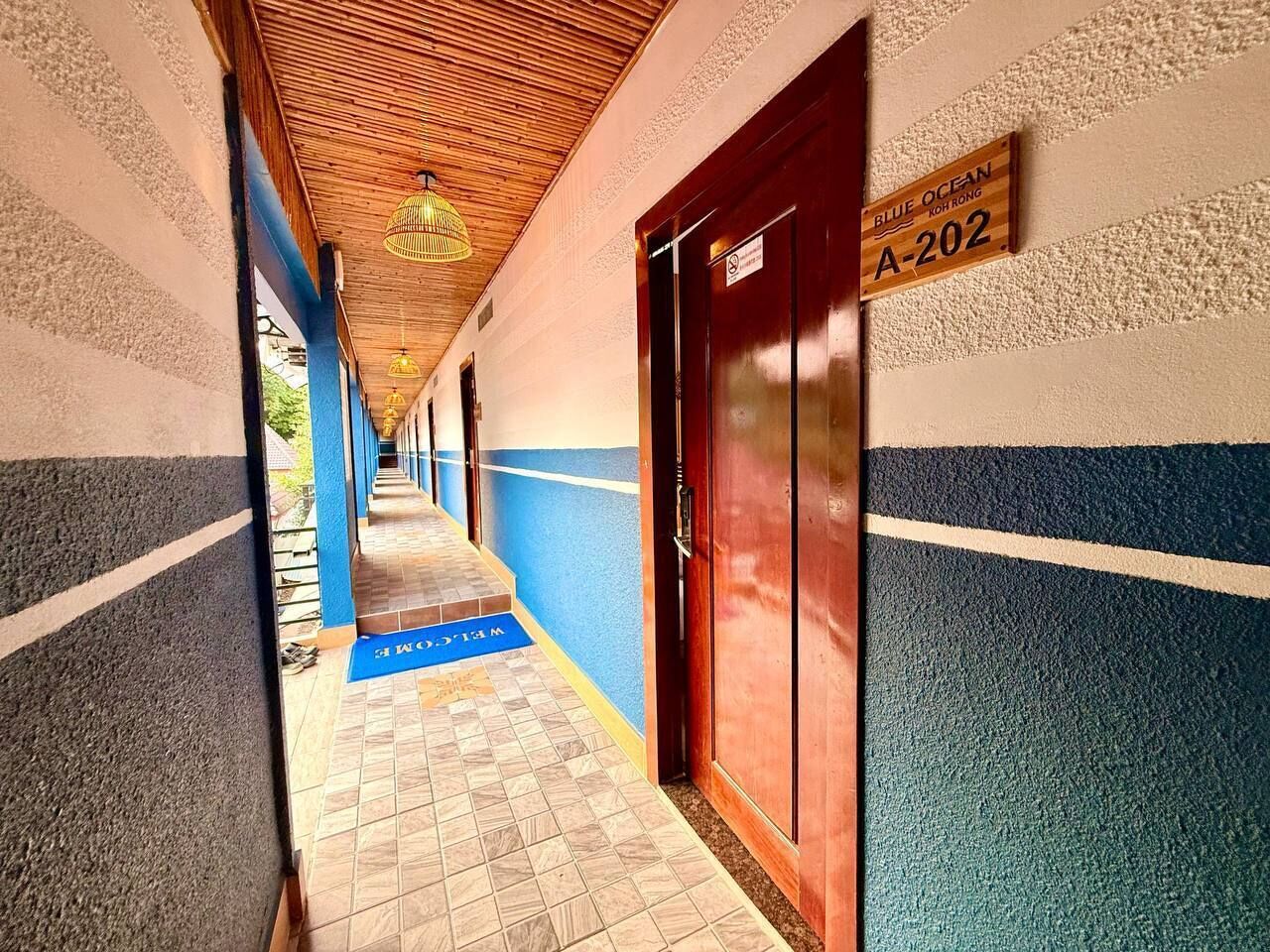 Um corredor com parede listrada em azul e branco, teto de madeira e um tapete azul que leva a um elevador identificado como 'A-202'.