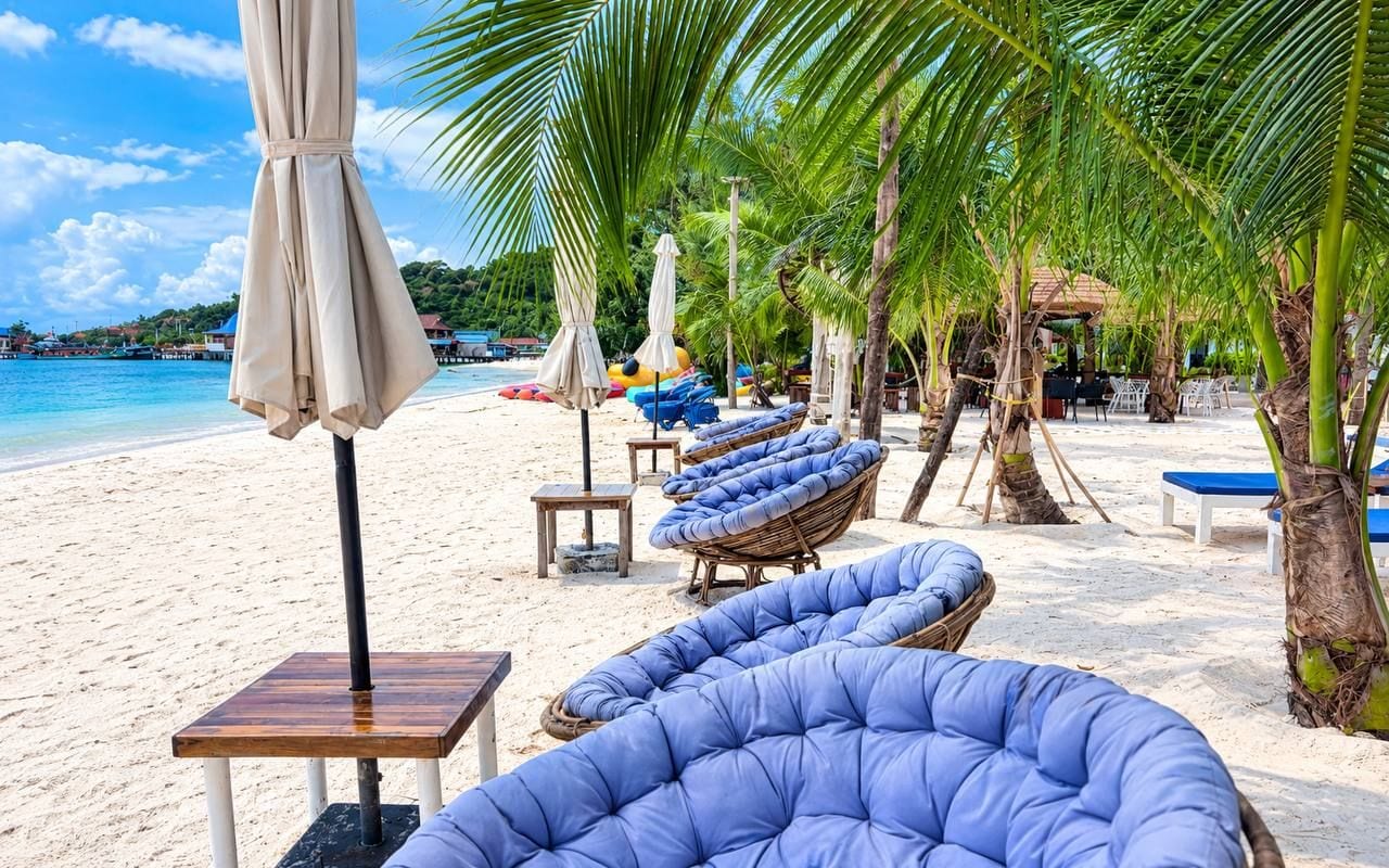 A beachside lounge area with cushioned seating, umbrellas, and a view of the ocean.