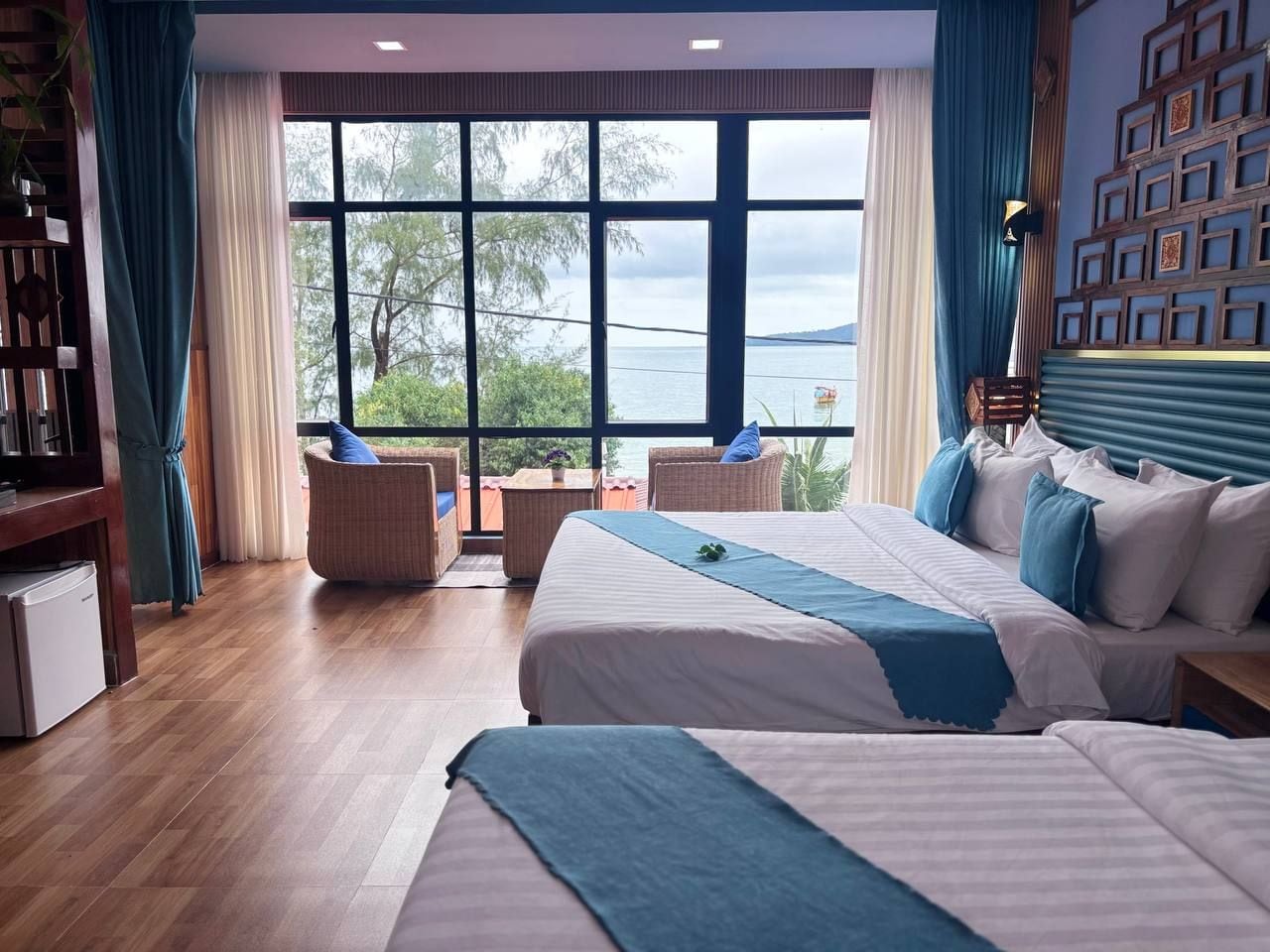 Une chambre d’hôtel avec une grande fenêtre, deux lits, une petite table et un coin salon avec des chaises.