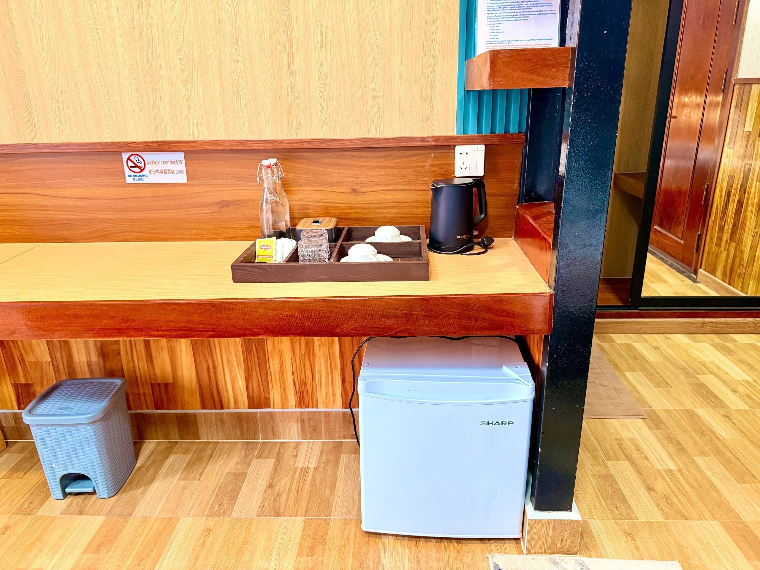 Bancada de recepção de madeira com um aviso de proibido fumar, chaleira, bandeja com saquinhos de chá, cafeteira e uma lixeira.