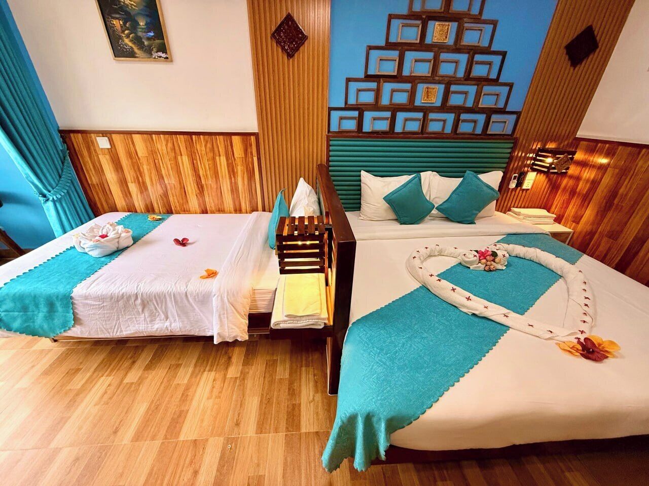 Ein Hotelzimmer mit zwei Betten, Holzboden, einer Wanddekoration und einem blauen Vorhang.