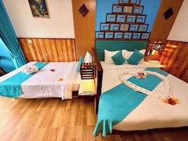 A hotel room with two beds, wooden flooring, a decorative wall, and a blue curtain.