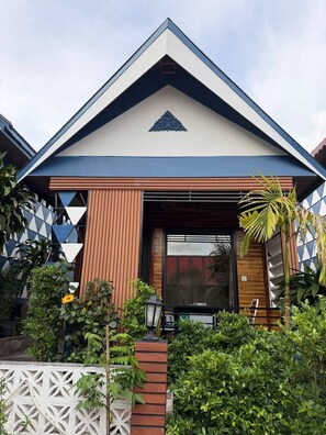 A modern house with a triangular roof, a wooden facade, and a white fence.