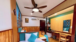 Habitación de hotel con cama, escritorio, silla, ventilador de techo y una pequeña kitchenette.