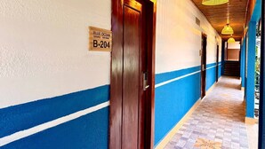 Un pasillo de hotel con una decoración en tonos azul y blanco, una puerta de madera con la leyenda 'B-204' y lámparas colgantes.
