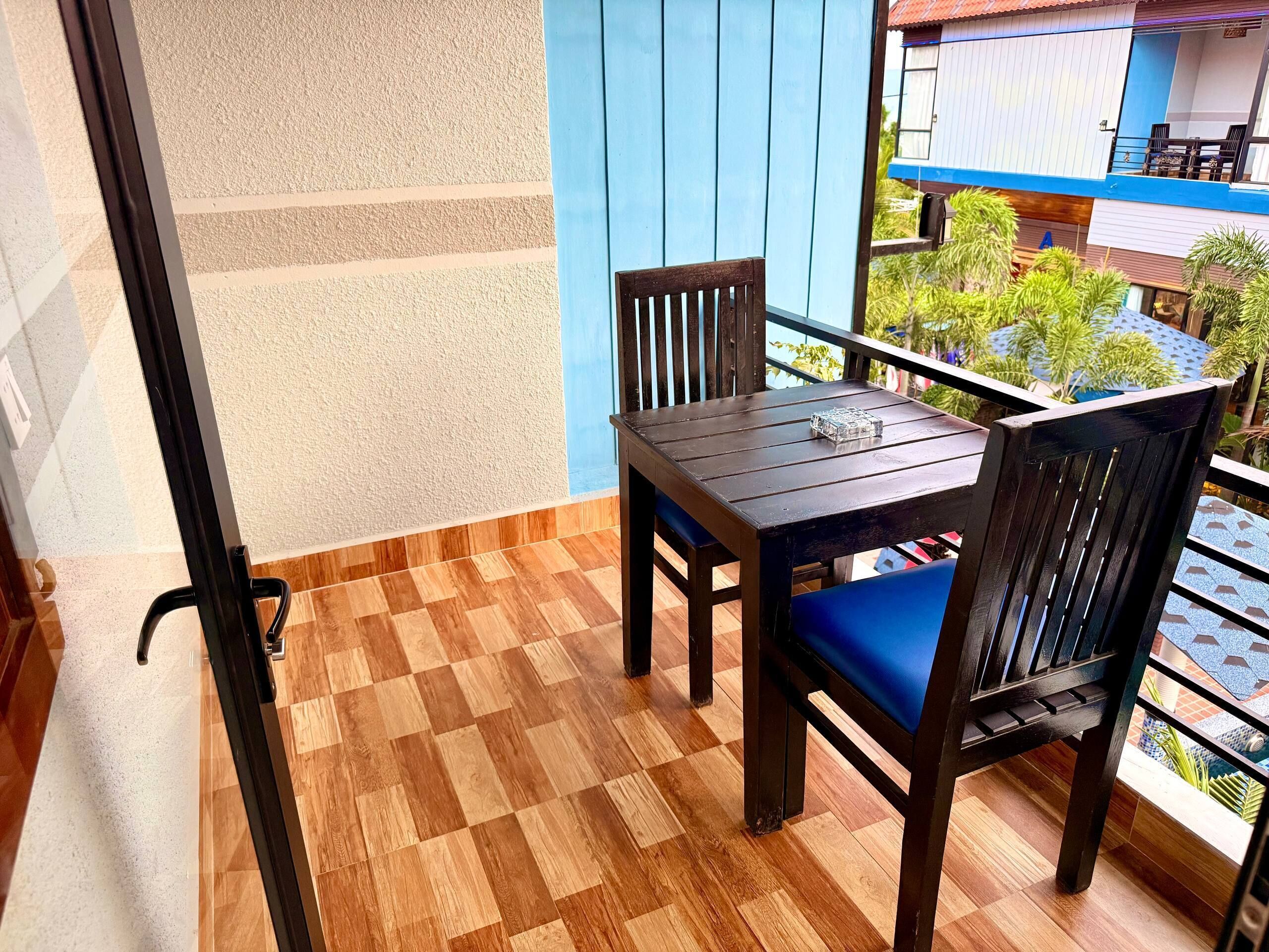 A balcony with a wooden table and chairs, a view of the surrounding buildings, and a checkered floor.