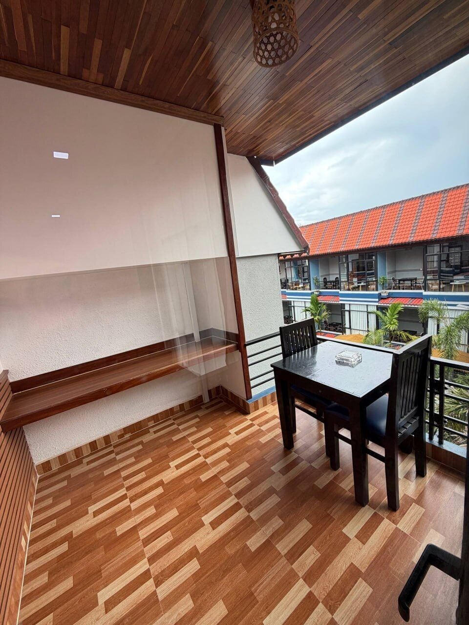 A balcony with a wooden floor, a table with chairs, and a view of a building with red tiles.