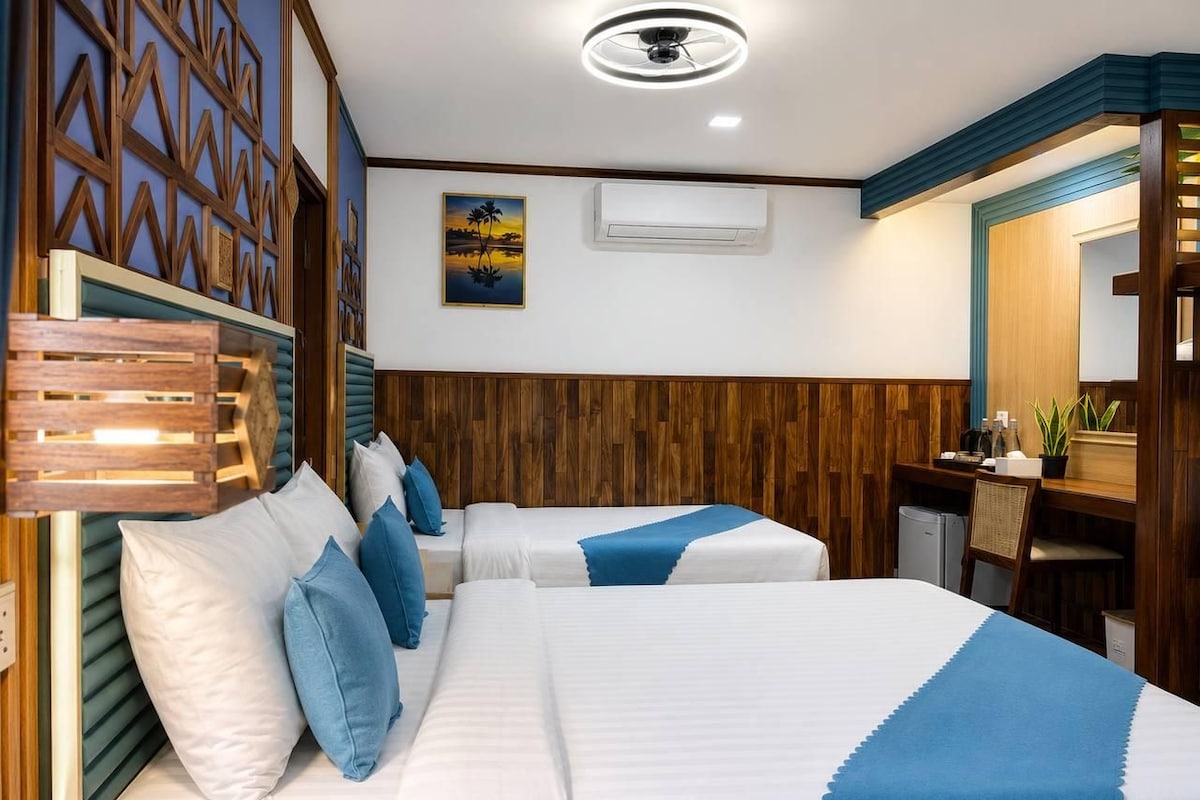 Habitación de hotel con dos camas, un escritorio, una silla y una pequeña cocina.