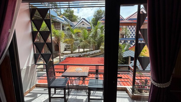 Un balcón con una mesa y sillas, vista a un área residencial con casas y palmeras.