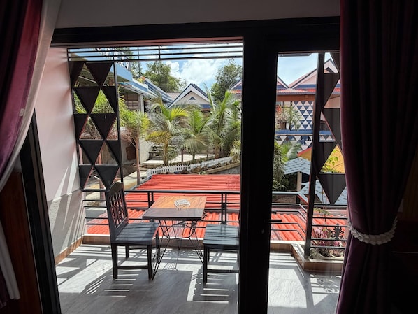 A balcony with a table and chairs, a view of a residential area with houses and palm trees.