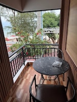 Un balcón con una mesa redonda y sillas, vista a un jardín con flores rojas y suelo de madera.