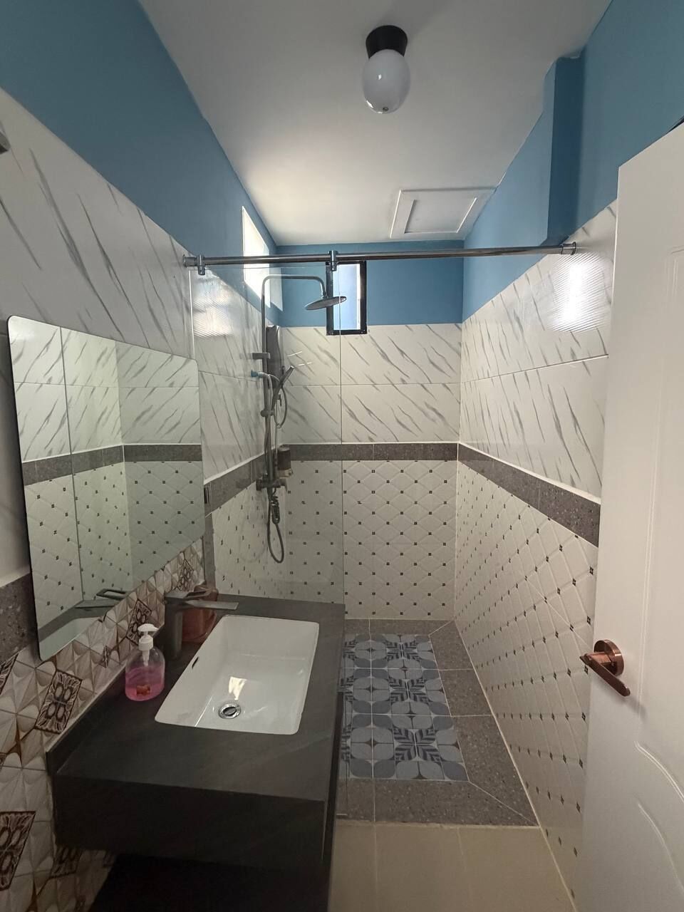 A bathroom with a sink, mirror, shower, and tiled walls.