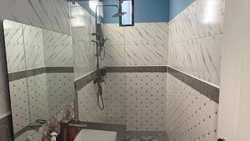 A bathroom with a sink, mirror, shower, and tiled walls.