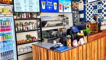 A coffee shop interior with a wooden counter, shelves stocked with beverages, a menu board, and a refrigerator with drinks.
