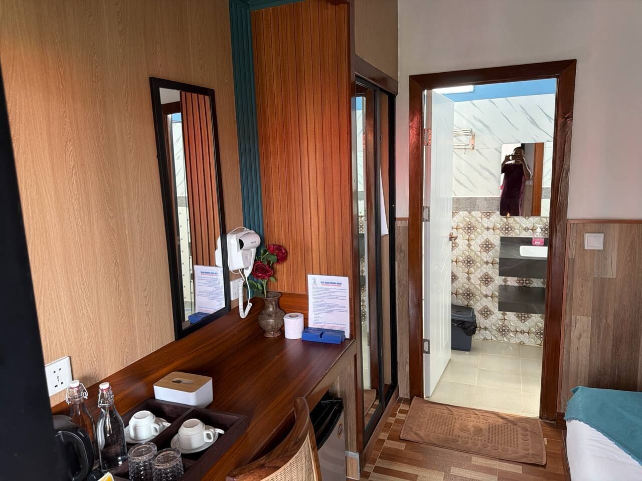 A hotel room with a wooden desk, a mirror, a bathroom visible through an open door, and a tiled floor.