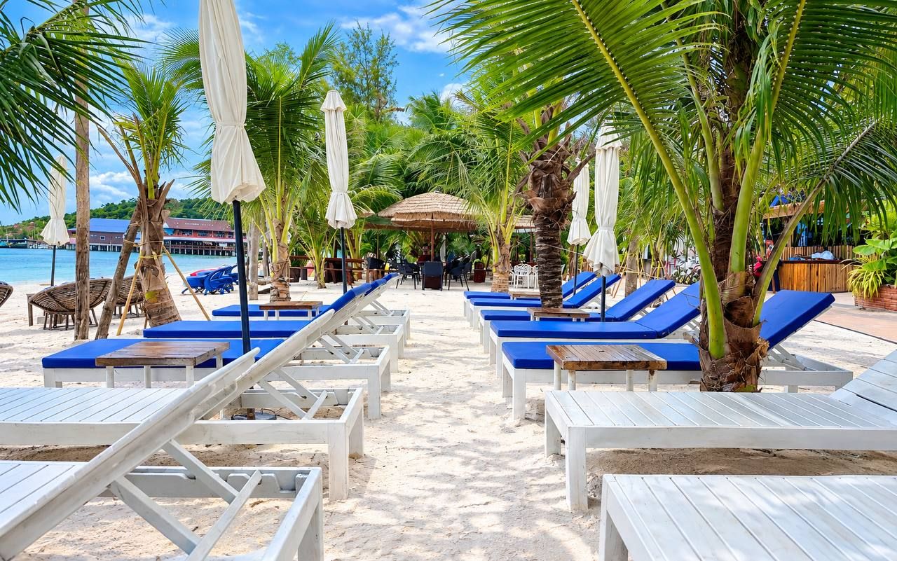 Un espace de détente aménagé au bord de la plage, avec des chaises longues et des parasols, une terrasse en bois et une vue sur la mer.