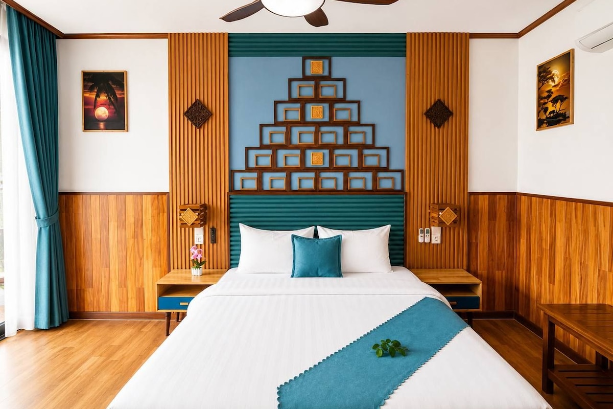 Habitación de hotel con cama, paneles de madera, ventilador de techo y una obra de arte en la pared.