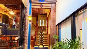 Entrada de un hotel con una escalera que lleva al interior, un letrero con la letra 'B' y una planta en maceta a la derecha.