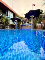 Una piscina con agua azul cristalina, rodeada por un edificio de fachada con azulejos y una bandera en la parte superior.