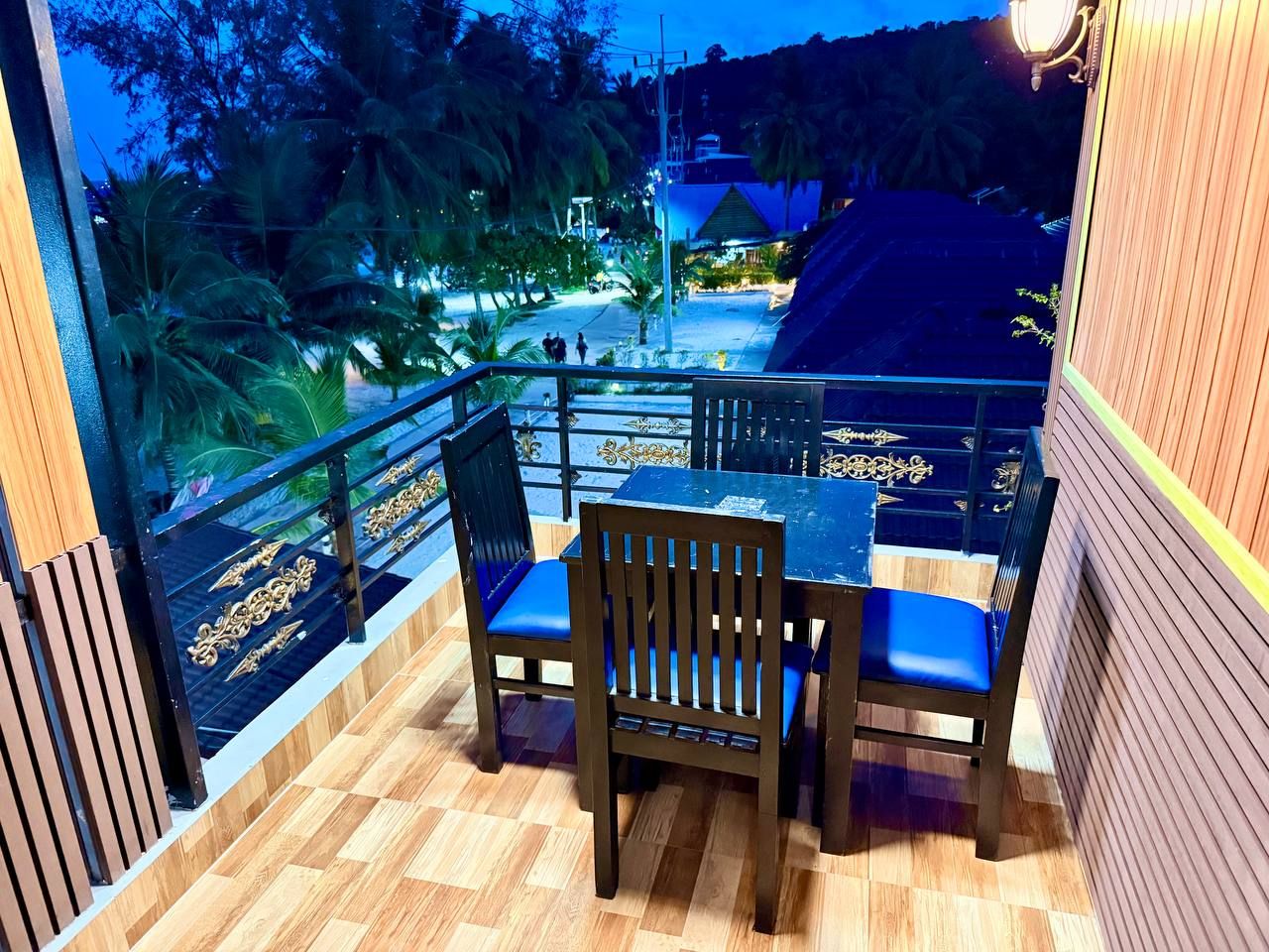 Un balcón con piso de madera, dos sillas con cojines azules y una mesa.