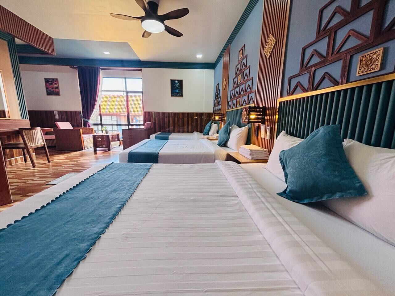Habitación de hotel con una cama grande, un escritorio y una silla. Hay un ventilador de techo y una ventana con cortinas.