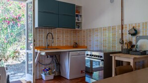 Une cuisine compacte comprenant un évier, une cuisinière et des placards, un coin repas avec une table et des chaises, et une vue sur un jardin grâce à une porte vitrée.