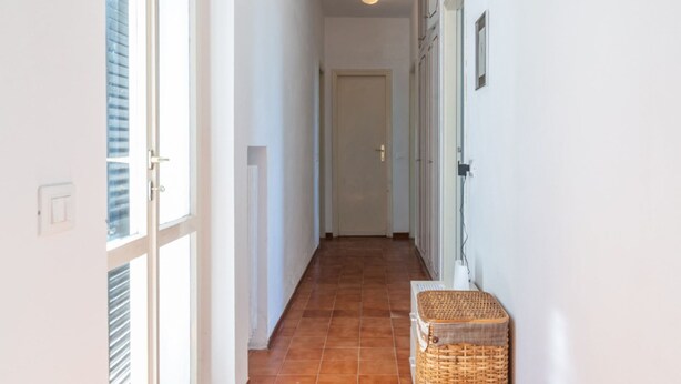 Un couloir avec une porte au fond, un panier sur la droite et une fenêtre sur la gauche.