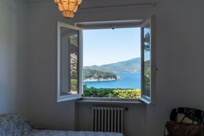 A bedroom with a window overlooking a coastal landscape. - Vista Sull'Enfola - Goelba (Portoferraio)