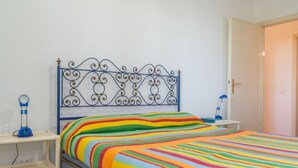 Un lit avec une couvre-lit rayé aux couleurs vives, une tête de lit en métal et deux lampes de chevet.