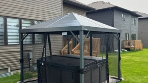 A covered hot tub with a metal frame and a roof, set on a lawn in front of a residential building. - Spacious Modern Orillia Family Retreat- Hot Tub (Severn)