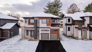 A modern multi-story residential building with a garage, surrounded by snow-covered ground. - Spacious Modern Orillia Family Retreat- Hot Tub (Severn)