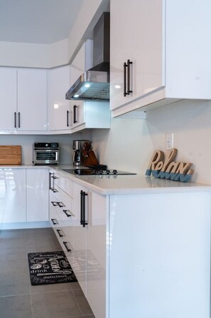 A modern kitchen with white cabinetry, a built-in oven, a stove, and a wooden cutting board. - Spacious Modern Orillia Family Retreat- Hot Tub (Severn)