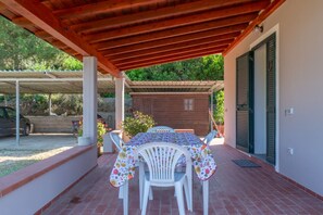 A covered patio with a table and chairs, a wooden structure, and a vehicle in the background. - AZIENDA AGRICOLA - APPARTAMENTO 2 (Capoliveri)