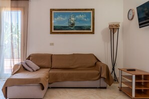 A living room with a sofa, a framed painting of a ship, a floor lamp, and a wooden side table. - AZIENDA AGRICOLA - APPARTAMENTO 2 (Capoliveri)