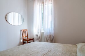 A bedroom with a bed, a chair, a round mirror, and sheer curtains. - AZIENDA AGRICOLA - APPARTAMENTO 2 (Capoliveri)
