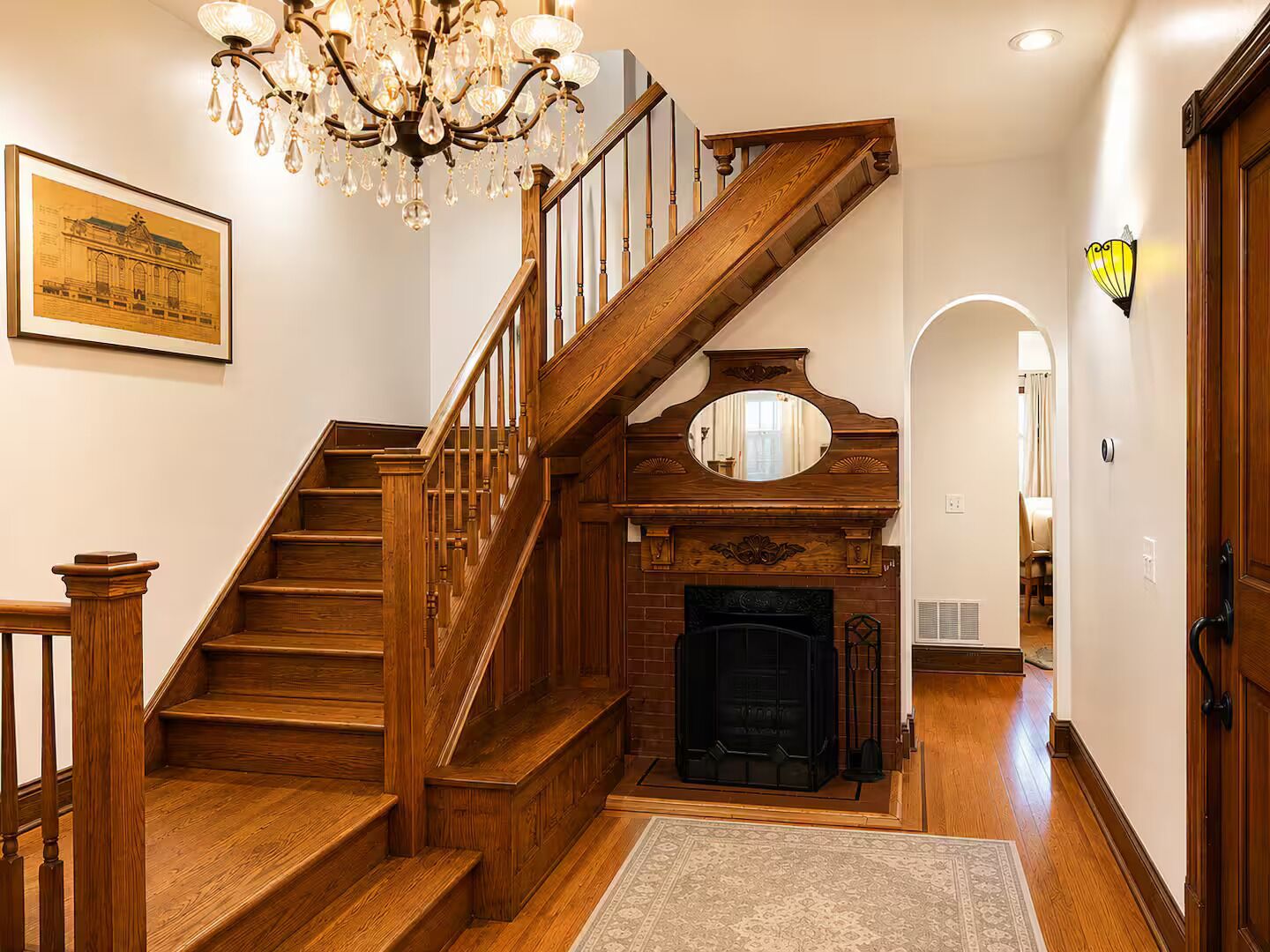 Una scala in legno conduce al secondo piano, con un camino e un lampadario.