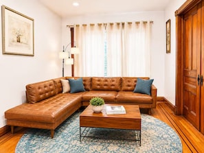 Ein Wohnzimmer mit einem braunen Ledersofa, einem Holztisch und einem gemusterten Teppich.