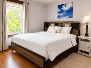 Ein Schlafzimmer mit einem Bett, einem Nachttisch, einer Lampe, einem Fenster mit Vorhängen und einem Himmelbild.