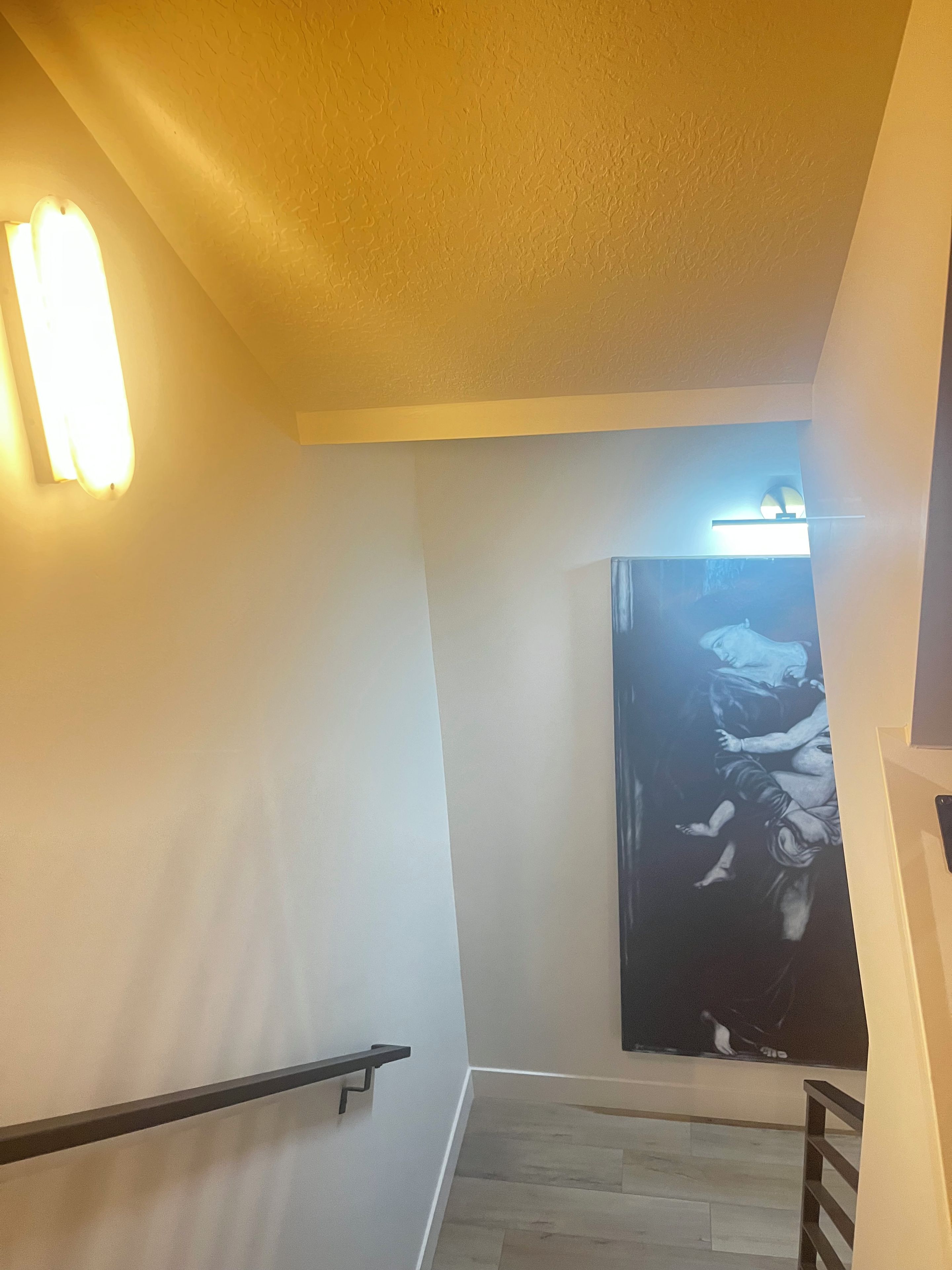 Eine Treppe mit Handlauf, eine Wand mit einer Leuchte und ein Bild von einer Figur.