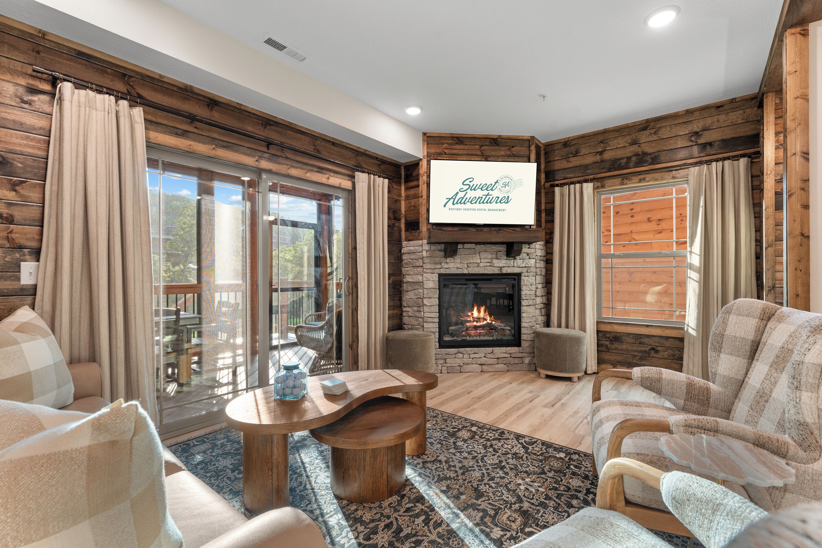 A cozy living room with a fireplace, comfortable seating, and a large window overlooking a deck.
